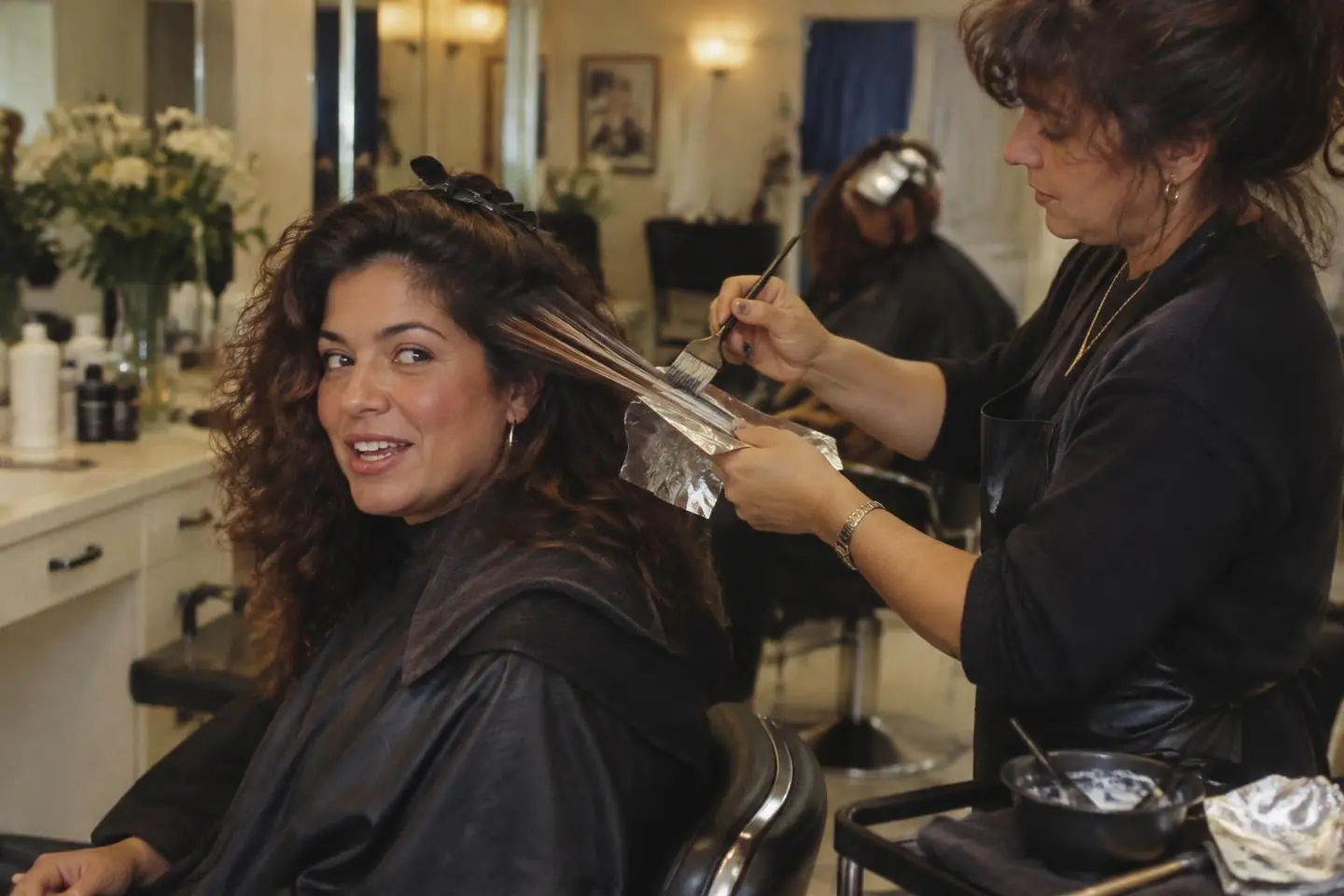 A colorist painting caramel balayage through a Brazilian-American client's dark wavy hair