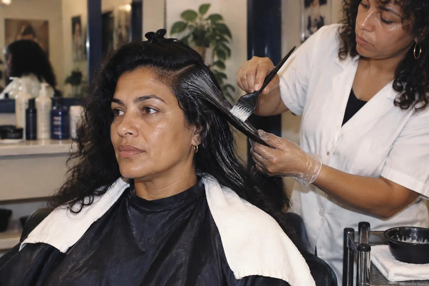 A stylist smoothing a conditioning treatment through a Brazilian client's sectioned textured hair