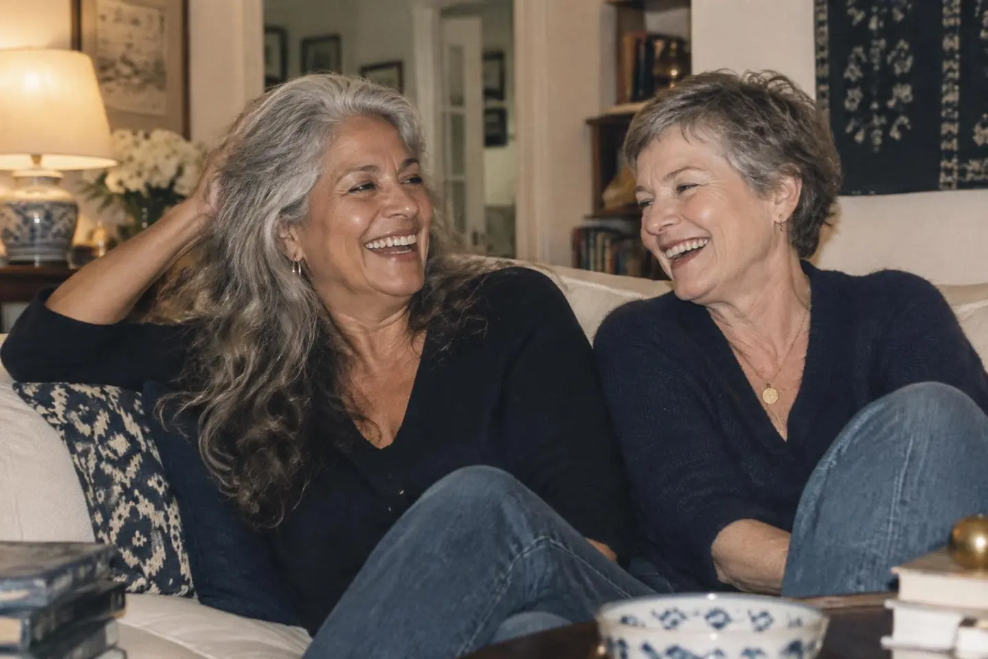 Two friends with long silver waves and a short salt-and-pepper crop laughing at home