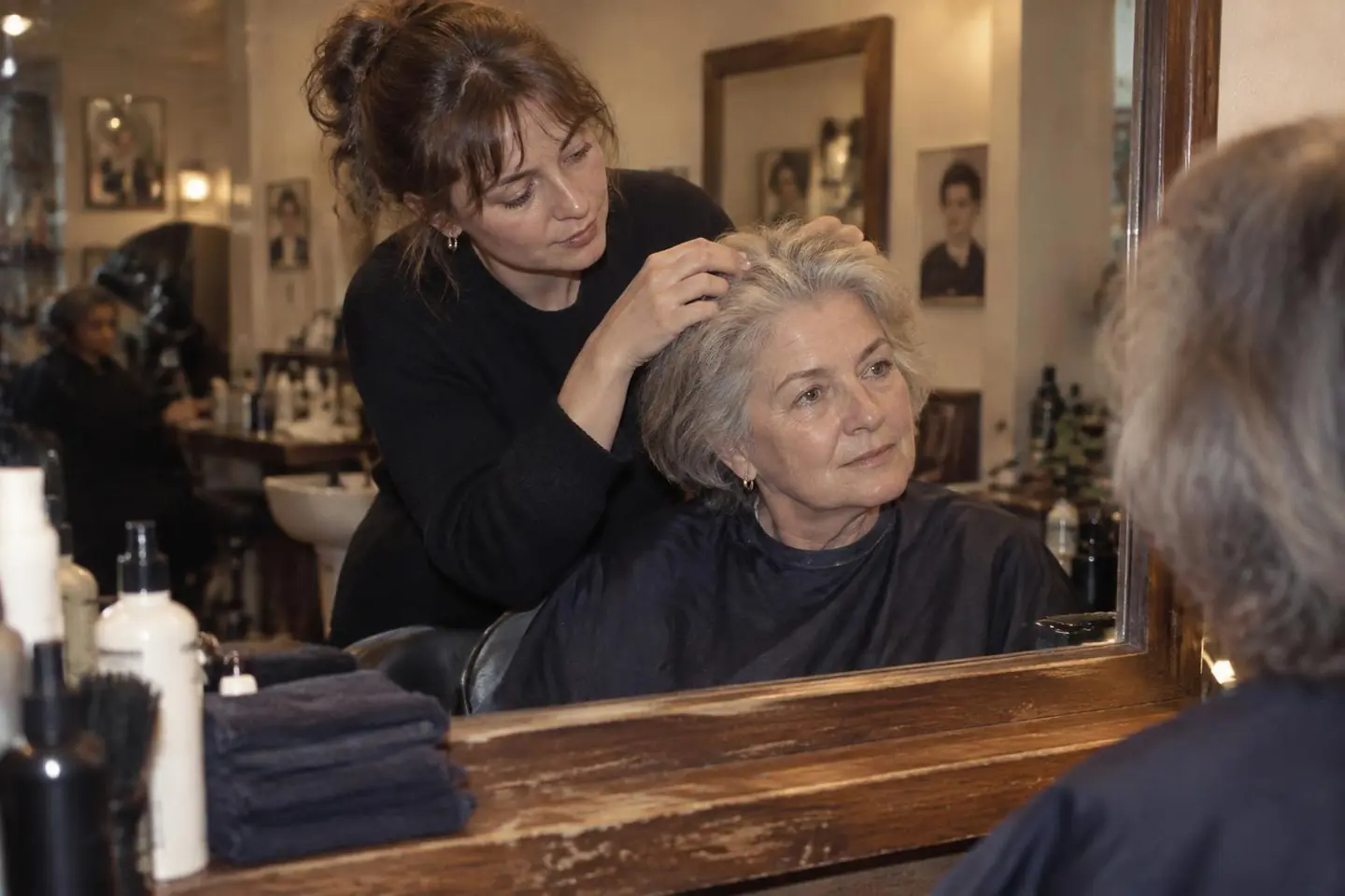A stylist checking the grey roots of an older client at the salon mirror